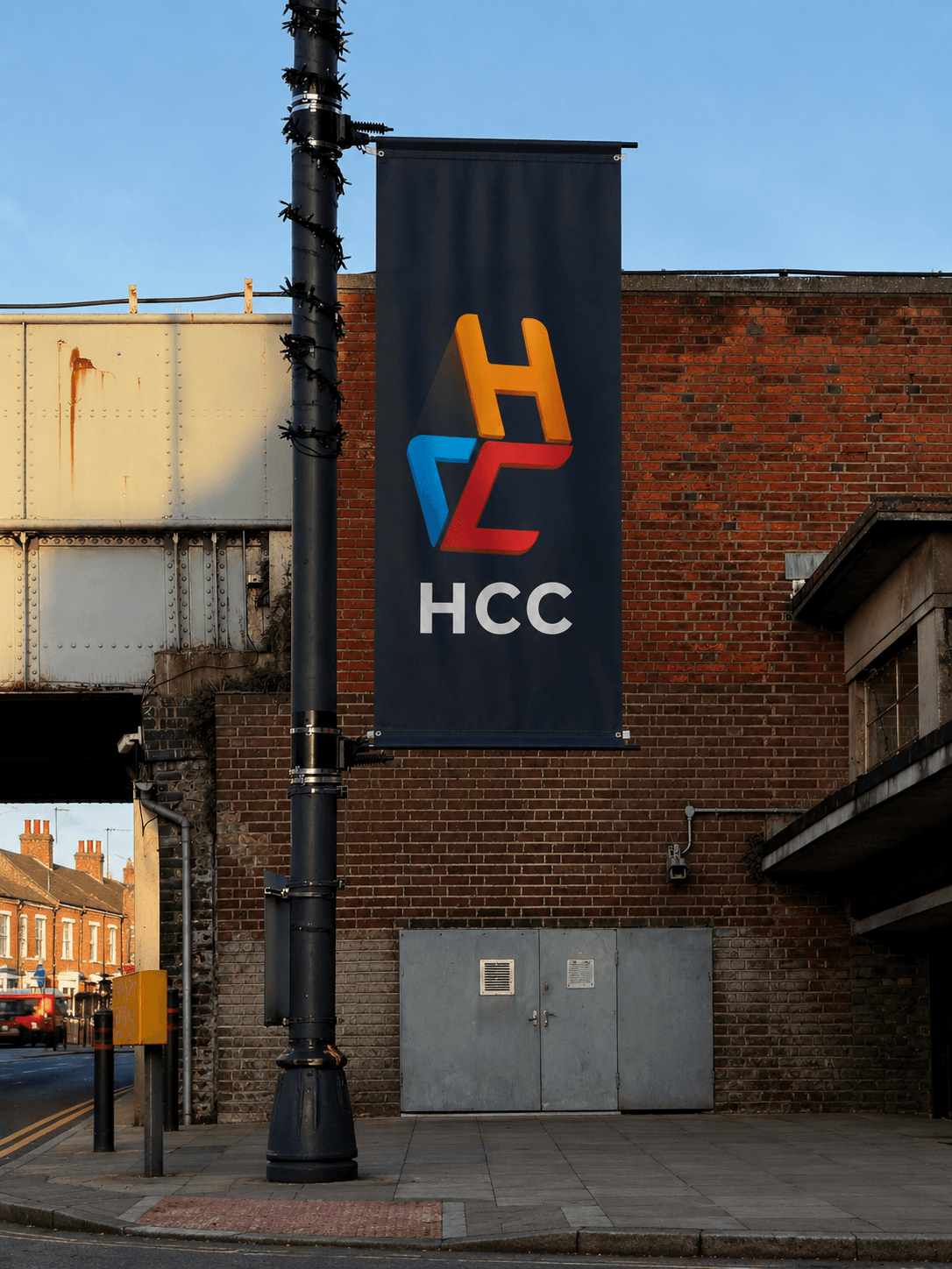 Black banner with a colorful HCC logo hanging from a lamppost on a city street.